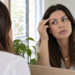 Eyebrow tattoo gone grey or too dark: correct it, remove it, or wait it out? Woman checks the colour and shape of her eyebrow tattoo in a daylight mirror.