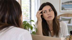 Woman checks the colour and shape of her eyebrow tattoo in a daylight mirror.