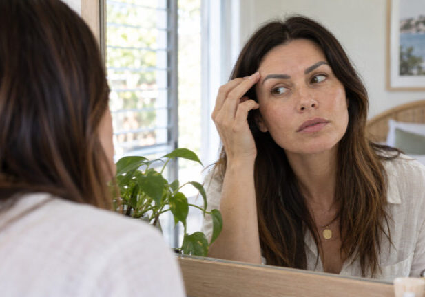 Eyebrow tattoo gone grey or too dark: correct it, remove it, or wait it out? Woman checks the colour and shape of her eyebrow tattoo in a daylight mirror.